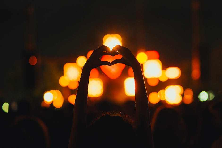Silhouette of hands forming a heart against vibrant concert lights at night.