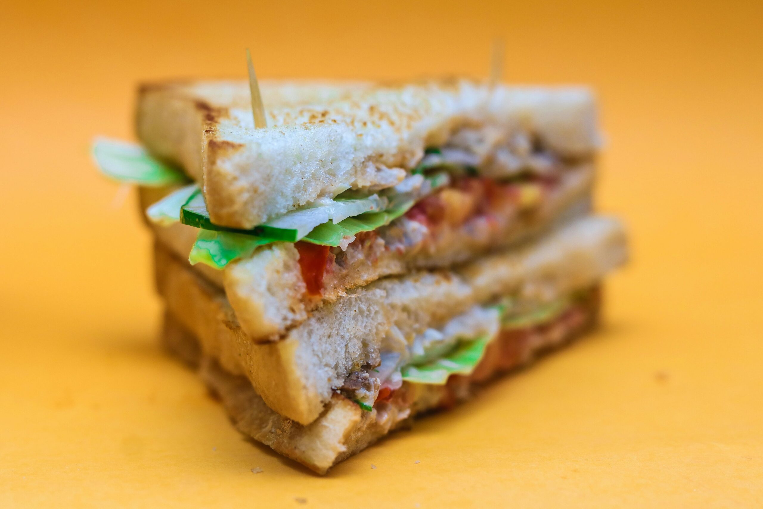 Close-up of a club sandwich with lettuce, tomato, and meat on a yellow background.